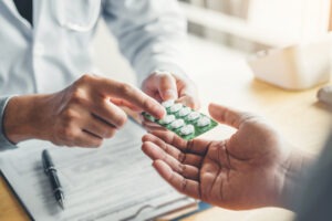 A doctor in a white coat hands a blister pack of white pills to a patient. A clipboard suggests a prescription, typical of an outpatient rehab in Nashville TN focused on supportive care and recovery.