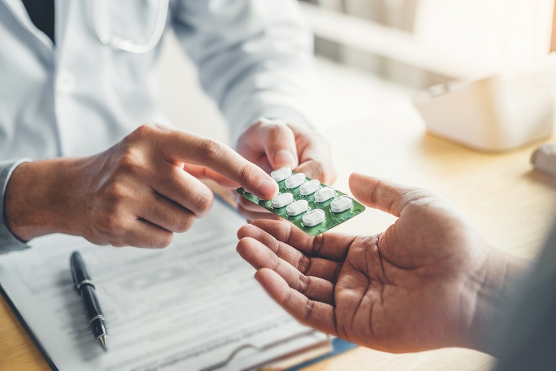A doctor in a white coat hands a blister pack of white pills to a patient. A clipboard suggests a prescription, typical of an outpatient rehab in Nashville TN focused on supportive care and recovery.