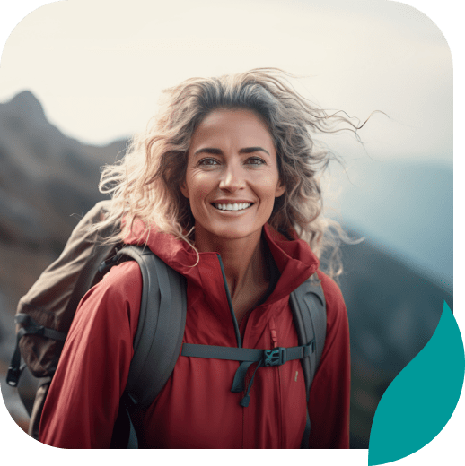 A smiling woman with wavy blonde hair wearing a red jacket and backpack stands outdoors in the mountains, with a blurred natural background and a decorative teal shape in the corner.