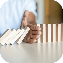 A hand stops a row of falling wooden dominoes, preventing the rest from toppling over, symbolizing intervention or the prevention of a negative outcome.